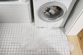 Front-load white washing machine leaking water and suds onto white tile floor.