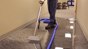 Technician vacuuming water in a carpeted hallway.