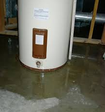 Tank water heater in unfinished basement, with water puddle under it.