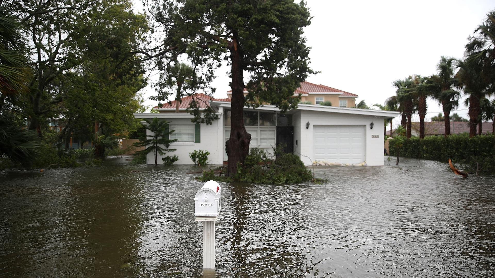 Flood waters in front of a white home, with water rising halfway up the post of the mailbox.