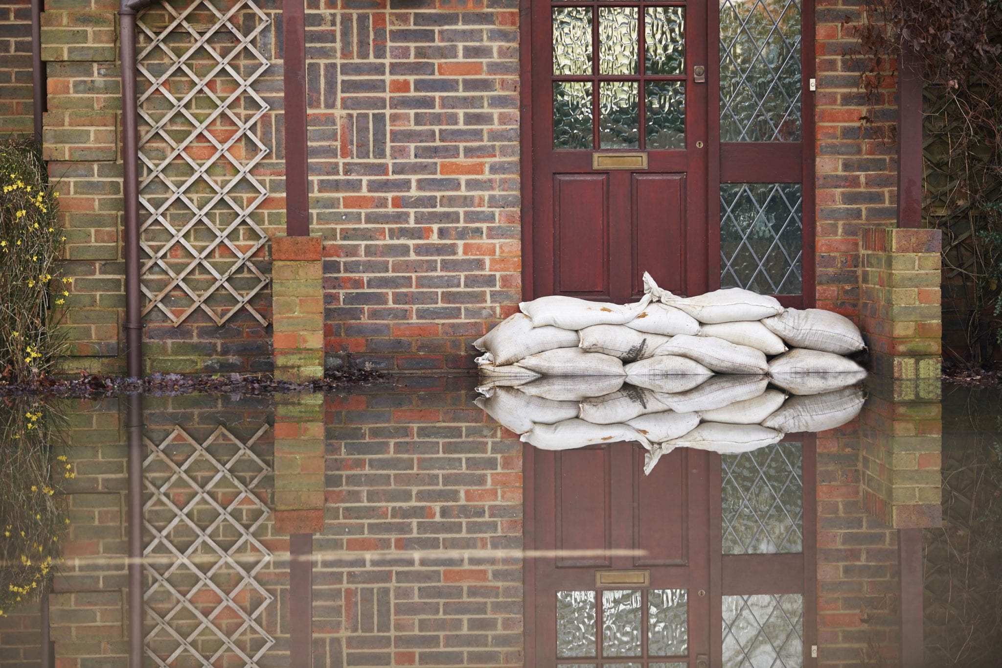 Sand bags piled up in front of a front door to a brick home, with water on the ground.