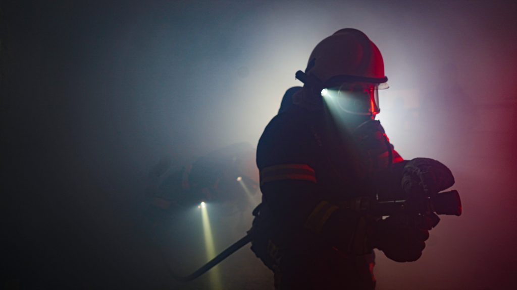firefighter in uniform moving through smoke with hose